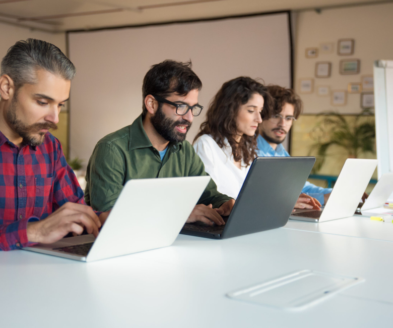 Startup team collaborating on project, using laptops at conference table. Business colleagues in casual working together in contemporary office space. Teamwork concept